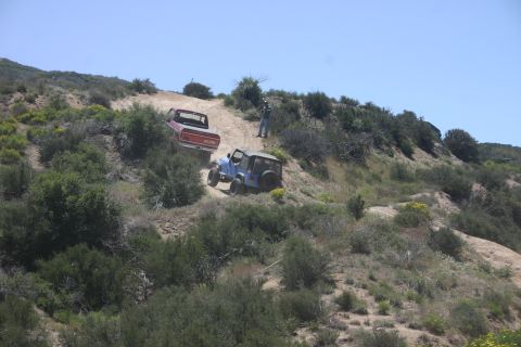 1991 Ford Bronco - Two off-road vehicles navigate a challenging dirt path on a sunny day.