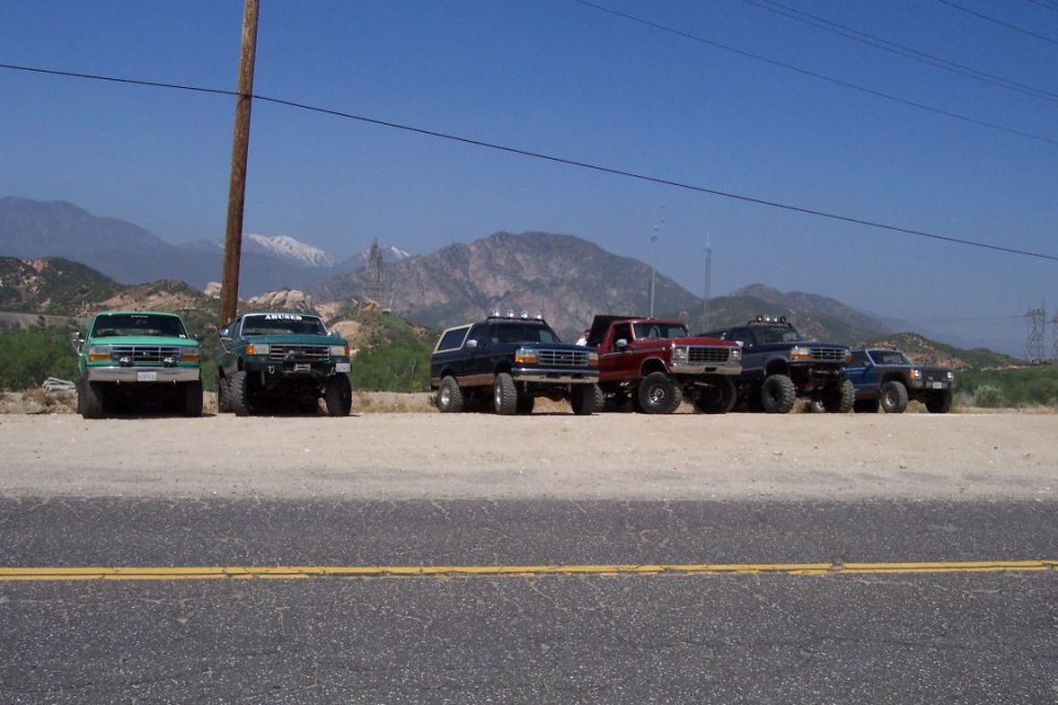 Several lifted trucks and SUVs parked in a line with mountains in the background