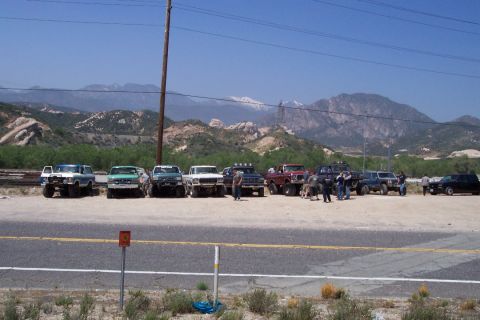 1995 Ford Bronco - A group of off-road vehicles are gathered in a dusty lot with a mountainous backdrop.