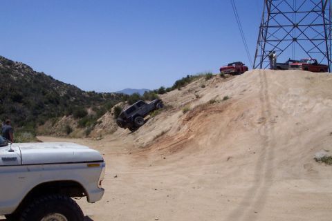 1995 Ford Bronco - Several vehicles navigate a steep, dusty incline under a clear blue sky, with a large power line tower visible.