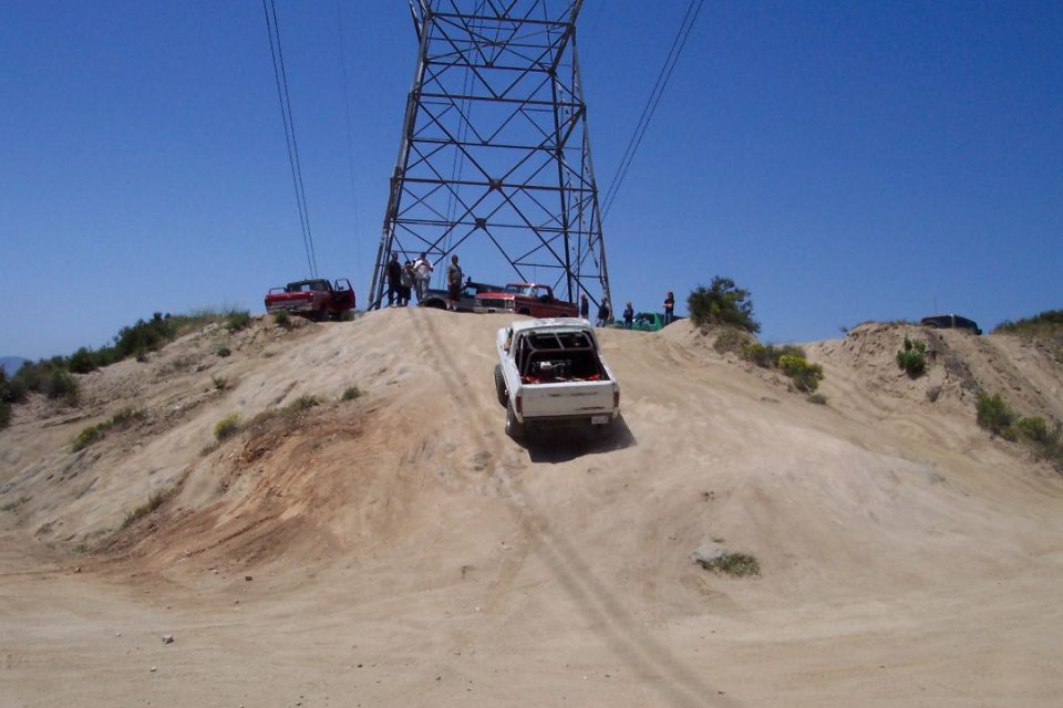 White off-road vehicle with roll cage driving up a dirt hill under a power line tower
