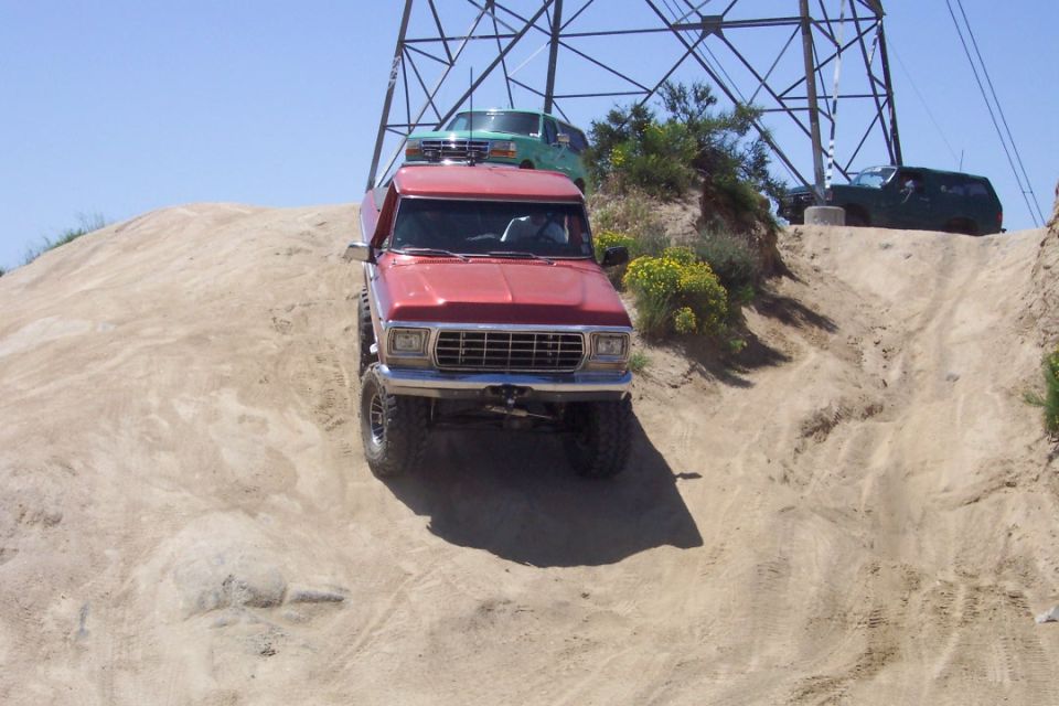 Red 1979 Ford F-Series pickup truck with green SUV on roof rack climbing sandy hill