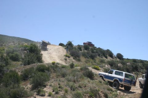 1991 Ford Bronco - Multiple SUVs navigate a challenging off-road trail on a sunny day.