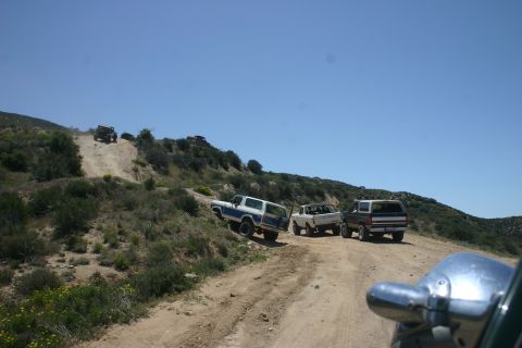 1991 Ford Bronco - Several off-road vehicles navigate a dusty trail on a sunny day.