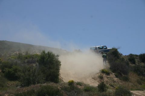 1991 Ford Bronco - A 1991 Ford Bronco navigates a dirt path, creating a significant dust cloud under a clear blue sky.