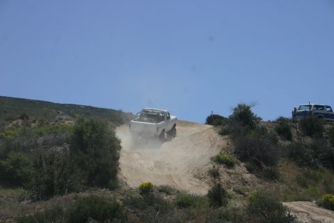 1991 Ford Bronco - Two vehicles navigate a dusty off-road trail under a clear blue sky.