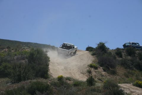 1991 Ford Bronco - Two off-road vehicles navigate a dusty trail on a sunny day with clear blue skies.