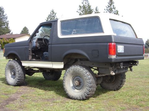 1988 Ford Bronco - This modified Ford Bronco features a lifted suspension and oversized off-road tires, with the driver's side door ajar.