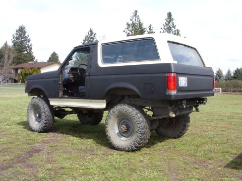 1988 Ford Bronco - This modified Ford Bronco, likely from the late 1980s, sits on a grassy field under a cloudy sky.