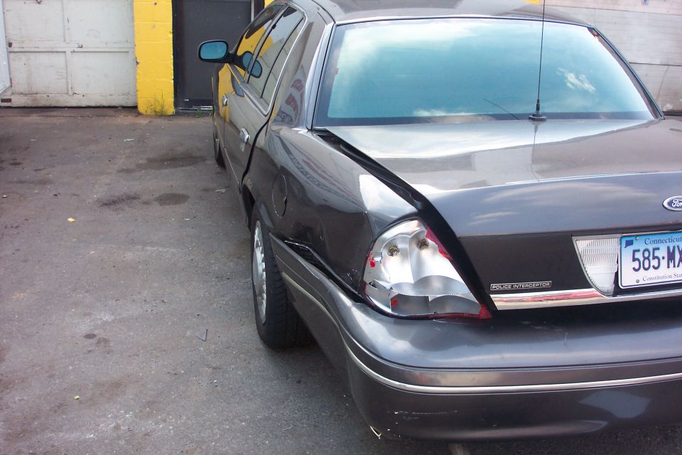 Dark sedan's rear end damaged, showing dented trunk and broken taillight. 1998 Ford Crown Victoria