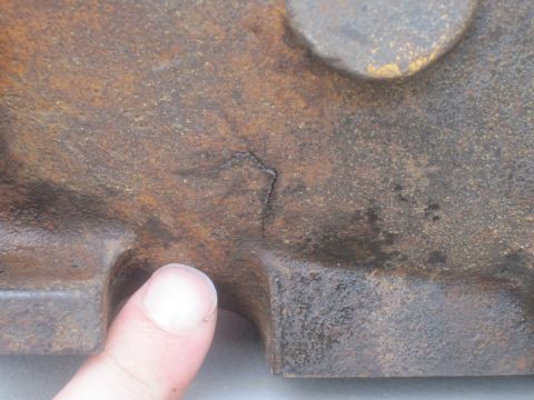 1979 Ford Bronco - A thumb points to a crack in a heavily rusted engine block casting.