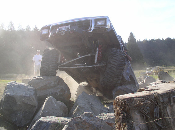 Off-road vehicle with large tires climbing over rocks, a person stands nearby
