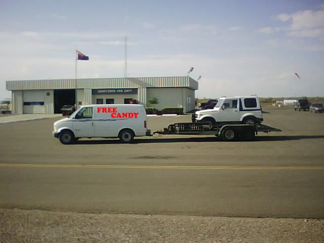 White van lettered FREE CANDY towing a white Suzuki Samurai on a flatbed trailer