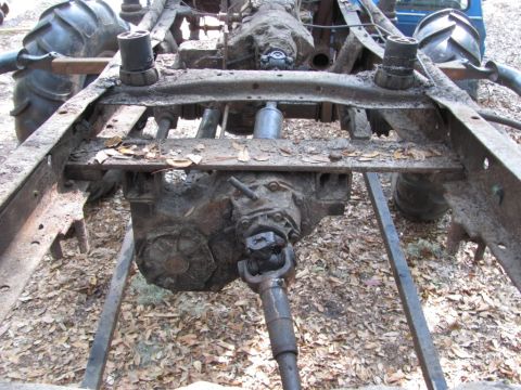 1982 Ford F-100 - Overhead view of a bare, leaf-strewn truck frame outdoors with the body removed, showing the transmission and transfer case sitting on the…
