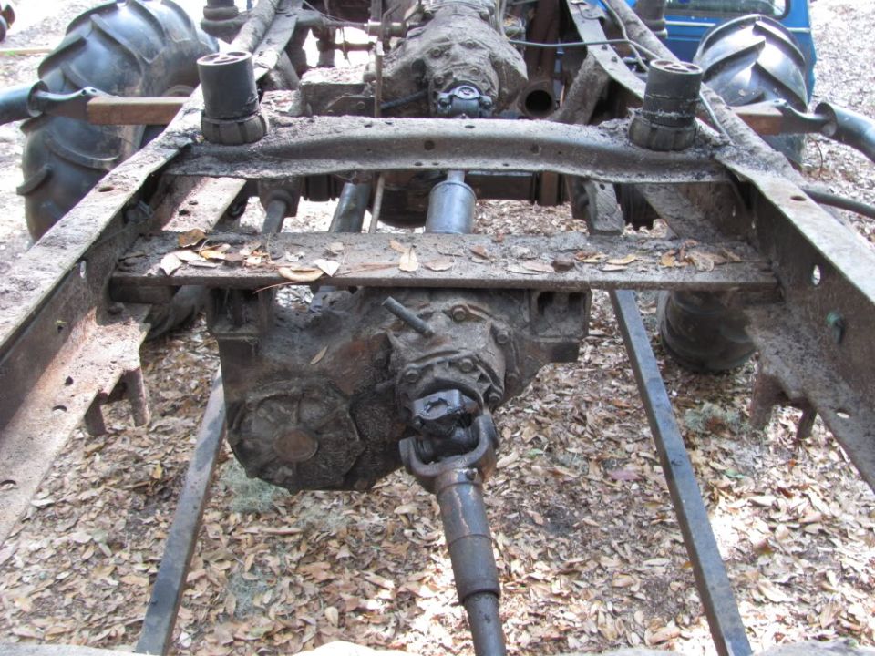 Bare rusty truck frame with transmission, transfer case and driveshaft, body removed, outdoors