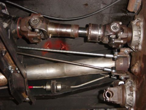 1982 Ford F-100 - Underbody close-up of a double-cardan driveshaft with twin U-joints running to a cast transfer case output, with a slip yoke and shift link…