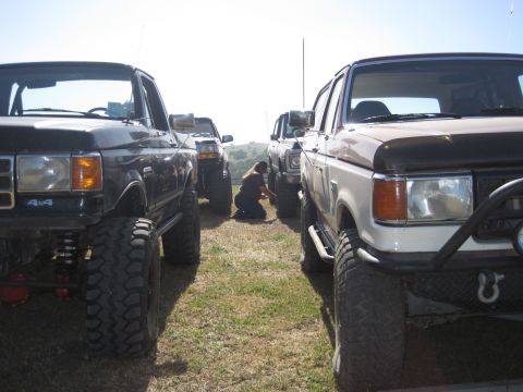 1989 Ford Bronco - Modified Ford Broncos from the late 1980s are lined up, with a person attending to one of the vehicles.