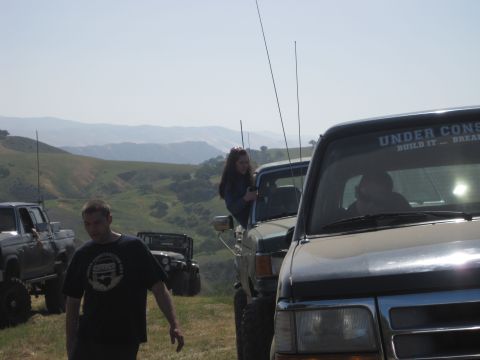 1989 Ford Bronco - A group of off-road vehicles are parked on a grassy hillside under a clear sky.