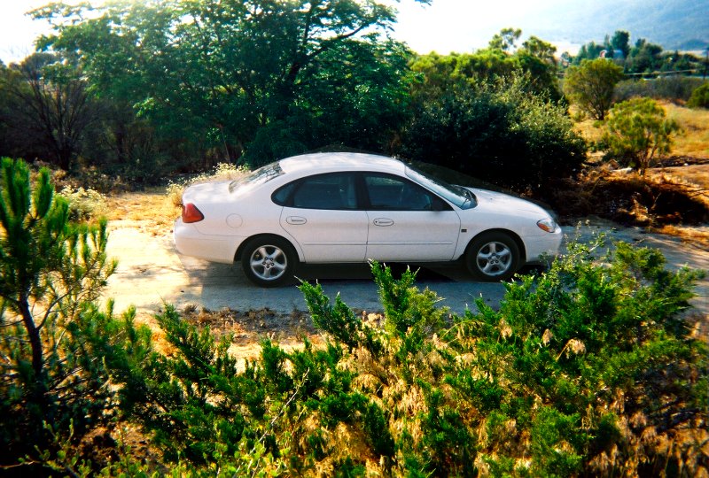 White 2000 Ford Taurus sedan parked on a dirt road, viewed from the side