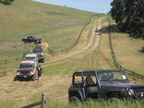 1989 Ford Bronco - A convoy of off-road vehicles navigates a winding dirt track through a rural, hilly landscape.