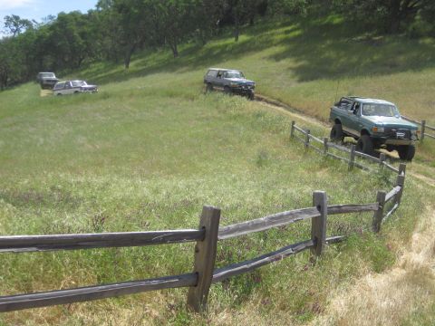 1989 Ford Bronco - A green 1989 Ford Bronco navigates a grassy hillside on a dirt track, with several other vehicles following.