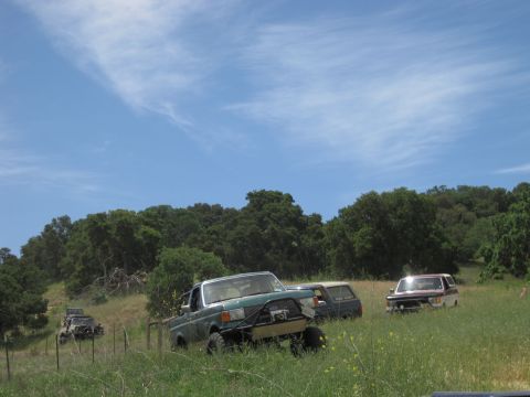 1989 Ford Bronco - Multiple off-road vehicles are parked in a field under a partly cloudy sky.