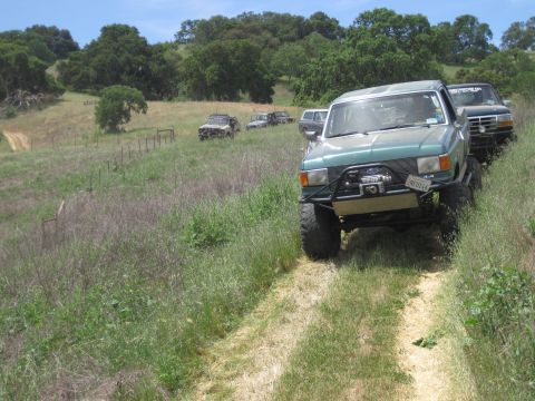 1989 Ford Bronco - A convoy of modified trucks navigates a rural, off-road trail under a clear sky.