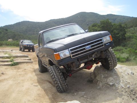 1989 Ford Bronco - A black 1987 Ford F-series truck navigates an off-road obstacle course with another SUV in the background.