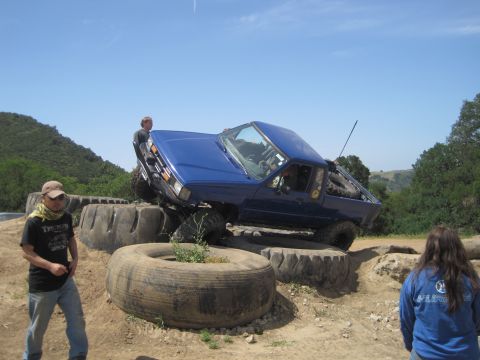 1989 Ford Bronco - Blue pickup truck attempts an off-road obstacle course constructed from large tires.