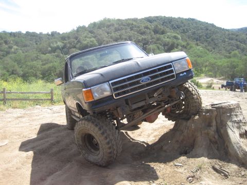 1989 Ford Bronco - This lifted Ford truck is navigating an obstacle course, with another vehicle in the background.