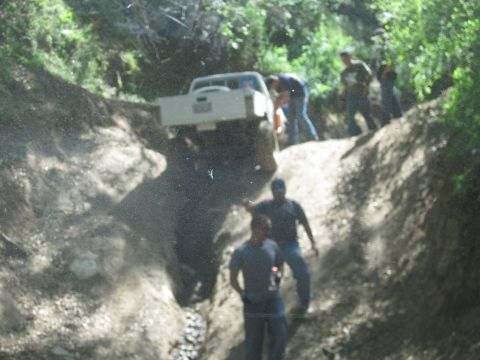 1989 Ford Bronco - A group of people watch as a white pickup truck maneuvers through a challenging off-road trail.