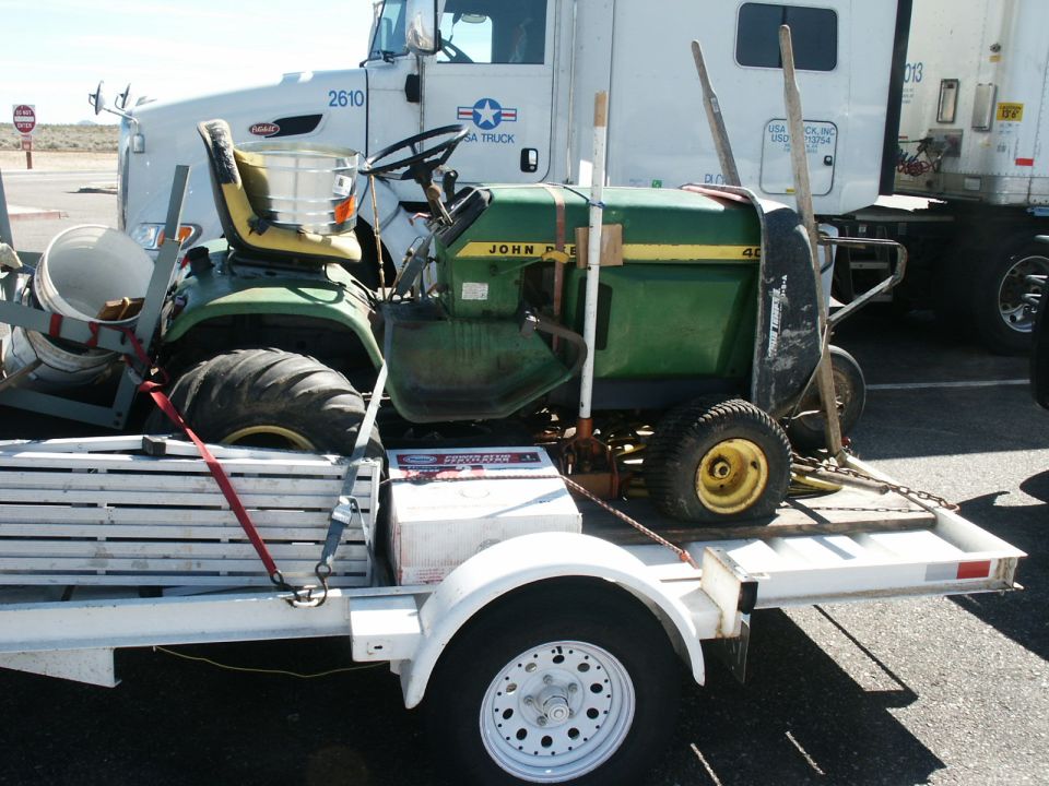 Green John Deere lawn tractor strapped on a white utility trailer at a truck stop