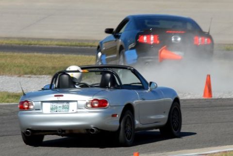 2007 Ford Mustang - A black Ford Mustang drifts on a race track, creating a cloud of dust and smoke.