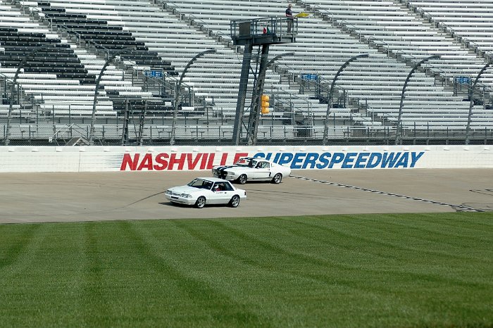 White 1987 Ford Mustang on racetrack with another Mustang behind it