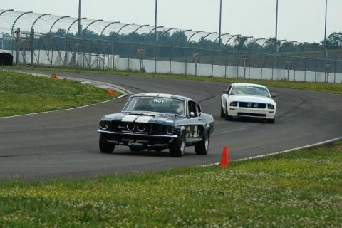 2007 Ford Mustang - Two Ford Mustangs compete on a race track, one classic and one modern.