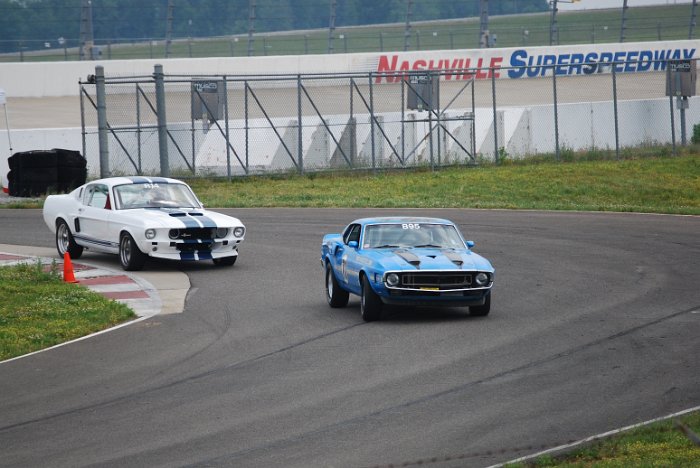 Blue 1969 Mustang racing on track, white Mustang behind it