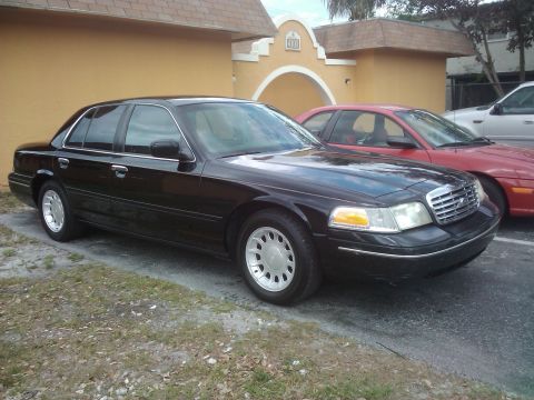 2001 Ford Crown Victoria - This black 2001 Ford Crown Victoria is parked next to a red car in front of a building.