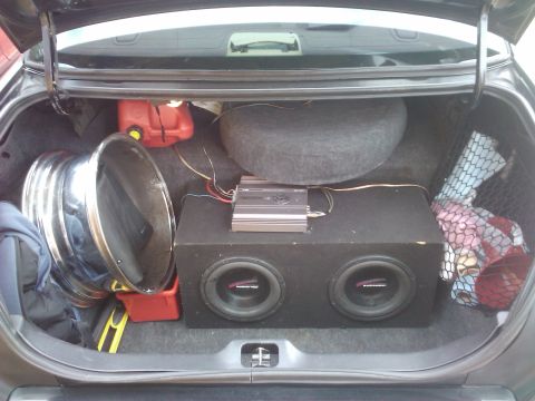 2001 Ford Crown Victoria - The trunk of a car contains audio equipment, a spare tire, a gas can, and a large chrome wheel.