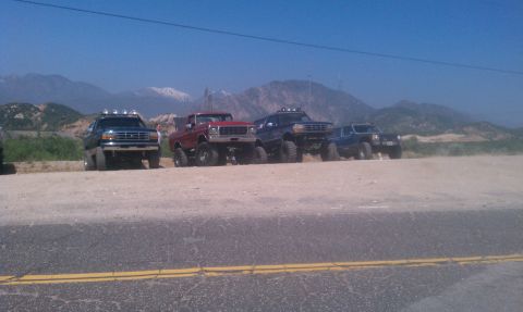 1978 Ford Bronco - A lineup of modified trucks sits parked on a dusty lot, ready for off-road adventure.