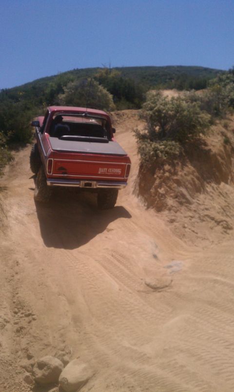 1978 Ford Bronco - This red pickup truck, possibly a 1978 Bronco, navigates a sandy off-road trail under a clear blue sky.