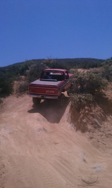 1978 Ford Bronco - Red pickup truck navigates a steep dirt trail under a clear blue sky.