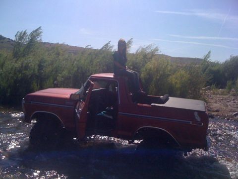 1978 Ford Bronco - A 1978 Ford Bronco is partially submerged in a shallow stream, with a person seated on its roof.