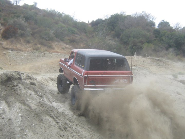 Red 1978 Ford Bronco kicking up dust while driving on a dirt hill