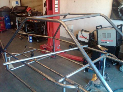 1995 Ford F-150 - A custom-built roll cage frame is shown in a workshop setting, surrounded by welding equipment and tools.