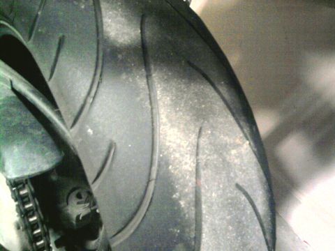 1985 Ford Crown Victoria LTD - Close-up of a motorcycle tire and chain guard, showing tread detail.