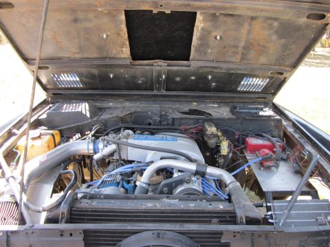 1971 Ford Bronco - The engine bay of a vehicle is shown with the hood open, revealing the engine and its components.