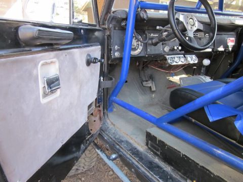1971 Ford Bronco - The interior of a 1971 Ford Bronco shows a blue roll cage, aftermarket steering wheel, and custom door panel.