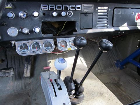 1971 Ford Bronco - Custom interior of a 1971 Ford Bronco features multiple shifters and aftermarket gauges on the dashboard.
