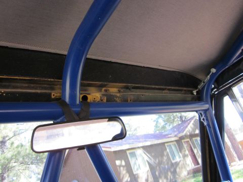 1971 Ford Bronco - Interior view of a vehicle's roll cage and rearview mirror, with a house in the background.