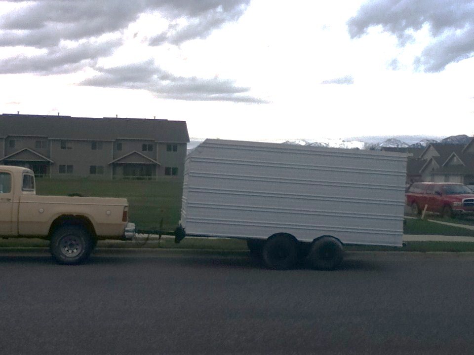 Tan pickup truck towing a white tandem-axle cargo trailer on a street